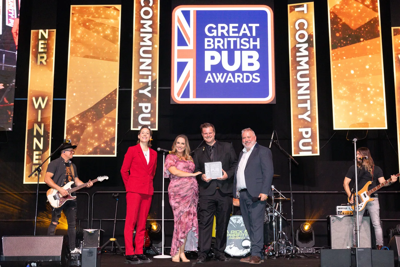 The Swan's award winners on stage beneath the Great British Pub Awards logo, with the house band either side